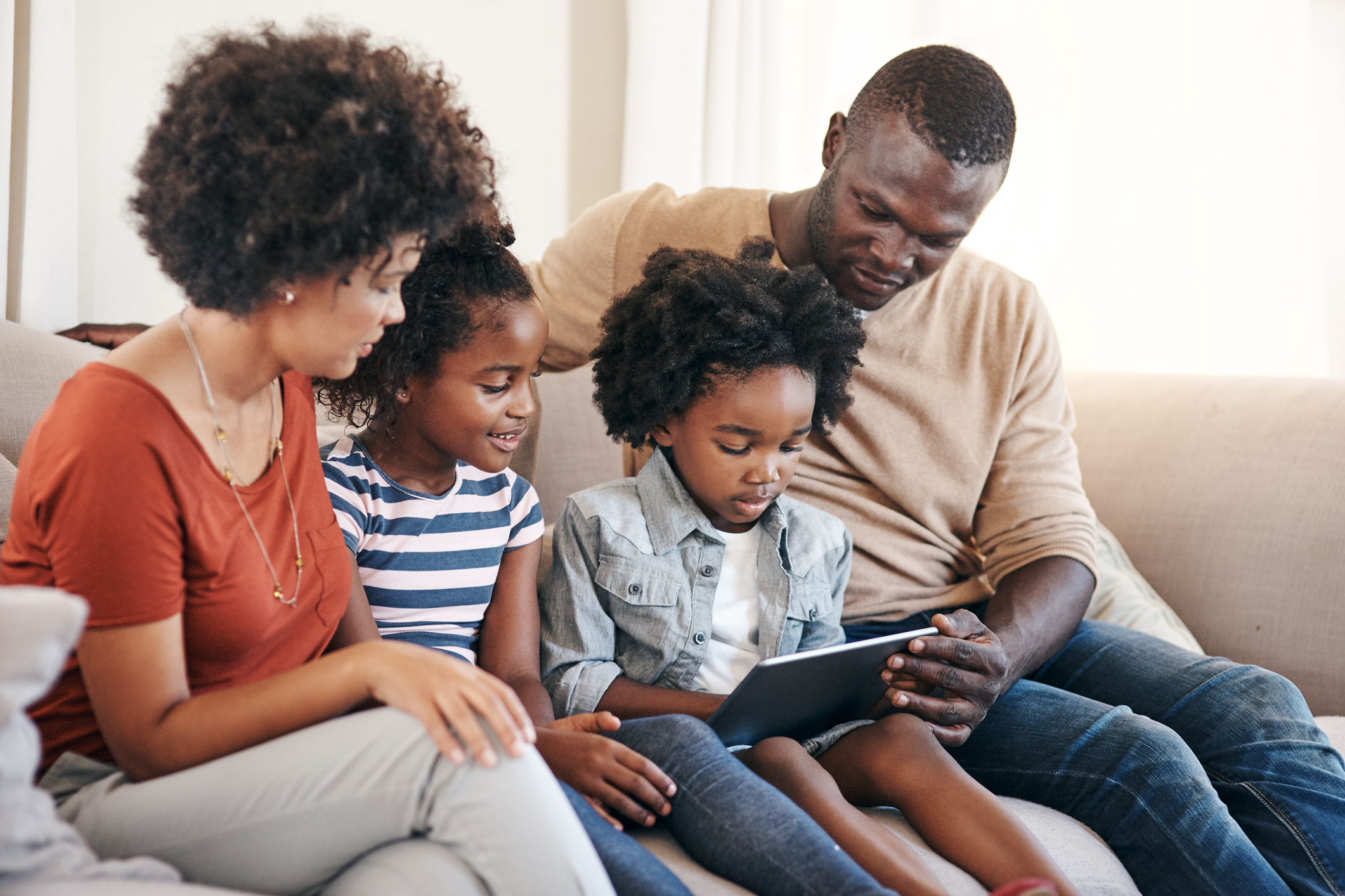 Shot of a cheerful young family spending time on a tablet together while being seated on the couch at home